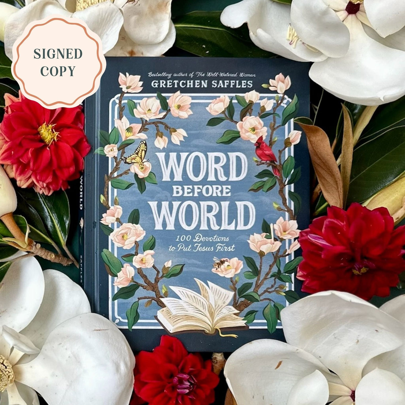 “Word Before World” devotional book by Gretchen Saffles displayed among white magnolia blooms and red flowers, with a “Signed Copy” badge in the corner.
